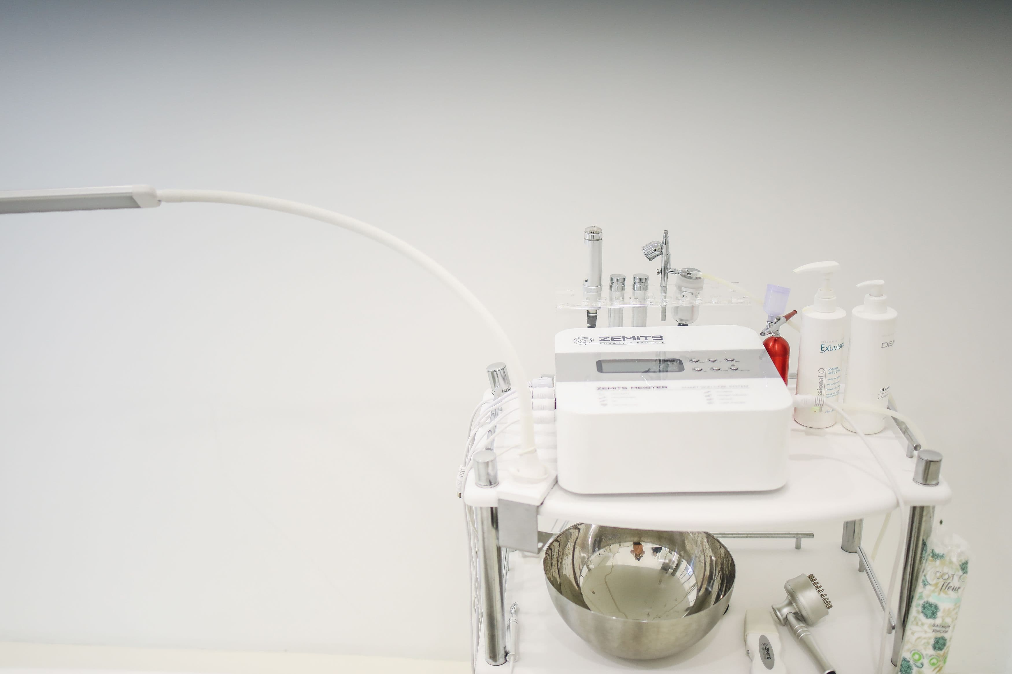 Skincare treatment equipment and bottles arranged on a white wheeled cart.